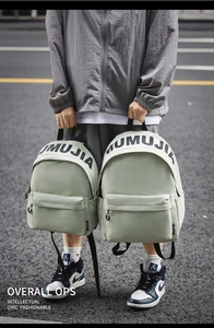 Detail of light green nylon backpacks with MUMUJIA logo held by a model in a street shot