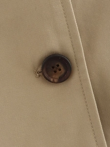 Detailed close-up of khaki twill fabric texture and brown tortoiseshell button on coat