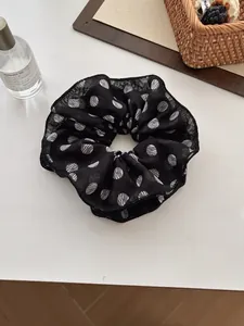 Detail of a chic black chiffon scrunchie with white polka dots on a marble tabletop