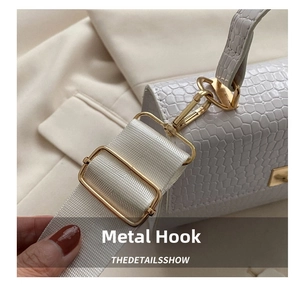 Close-up of white crocodile texture bag featuring gold metal hook and wide knit strap