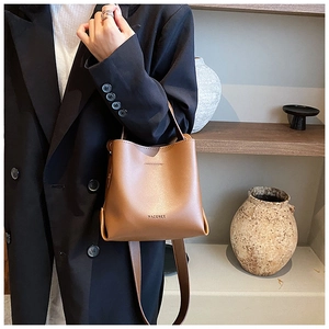 Detail view of brown leather bucket bag showing textured material and MACGNEE brand logo