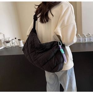 Detailed view of black quilted puffer tote bag worn by a model in a cozy cafe setting