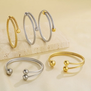 Detailed macro of woven stainless steel cable bangles with polished end caps on marble