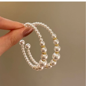 Detail of C-shaped hoop earrings featuring white pearls and gold beads on a silver needle