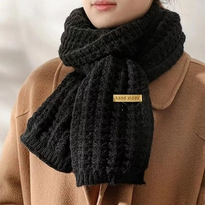 Close-up of thick black ribbed knit scarf with handmade gold tag on wool coat