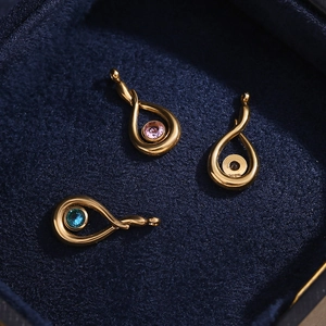 Detail of tear-shaped gold pendants with pink and blue zircons on dark velvet