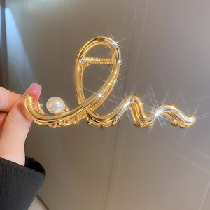 Detail of a wavy golden metal hair claw with a large pearl held by hand with star flare