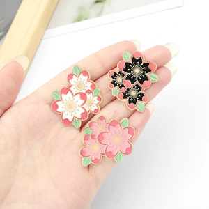 Nahaufnahme von drei bunten Kirschblüten-Emaille-Pins in der Hand für die Taschendekoration