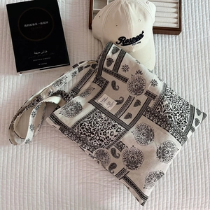 Close-up of paisley printed canvas tote bag styled with book and cap on white background