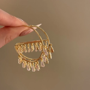 Detail shot of golden C-shaped tassel earrings with inlaid cubic zirconia crystals