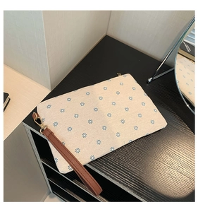 Detail of beige straw clutch bag featuring blue flower patterns and brown wrist strap