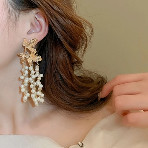 Close-up of elegant gold leaf earrings with white pearl tassels worn by a model