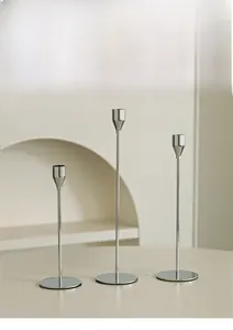 Close-up of three modern silver iron candlesticks set against an elegant minimalist background