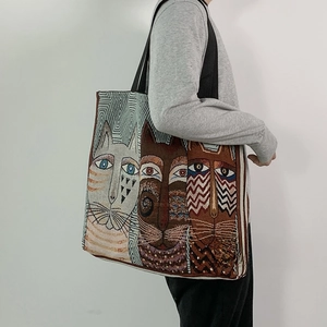 Side view of a large woven tote bag with artistic cat patterns and black shoulder straps