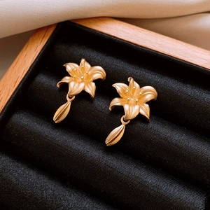 Macro boucles d'oreilles fleur de lys dorées avec pendentif feuille dans un écrin