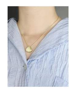 Detail shot of a minimalist gold shell pendant necklace on a blue textured shirt
