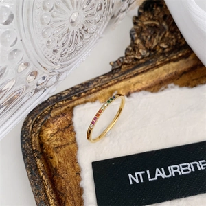 Close-up of gold-plated rainbow gemstone eternity ring on a white textured card