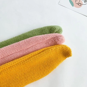 Close-up of three knitted baby scarves in green, pink, and yellow showing soft texture