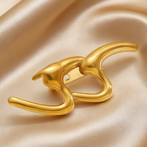Detailed view of a gold high-polish abstract S-shaped brooch on champagne silk background