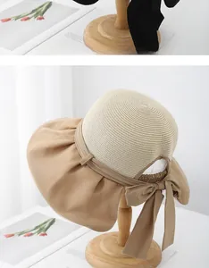 Detail of wide brim straw sun hat featuring a khaki fabric trim and large decorative bow