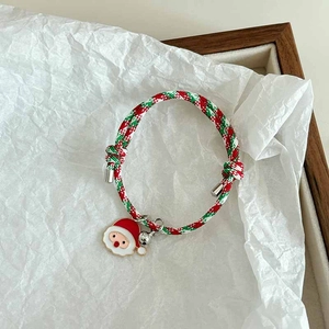 Detailed macro view of Christmas bracelet with Santa charm, bell, and red green woven cord