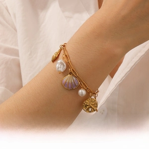 Detail of gold ocean charm bracelet with shell, pearl and starfish on model wrist
