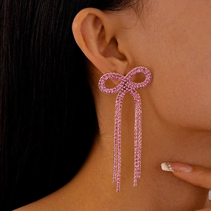 Boucles d'oreilles nœud rose avec strass et pompons portées par un mannequin de profil