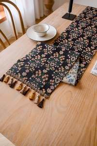 Detail of jacquard table runner with orange floral pattern and black base with tassels