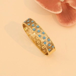 Close-up of gold hollow geometric flower bracelet with turquoise beads on peach background
