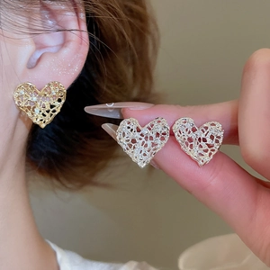 Detailed close-up of golden heart-shaped cutout earrings with intricate lace-like texture