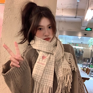 Plaid scarf with heart embroidery and tassels worn by a model in a cozy setting