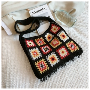 Detail of a handmade black knit tote bag with colorful granny square patterns and fringe