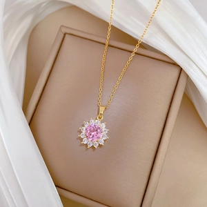 Close-up of gold sunflower pendant with pink crystal and tiny gems on beige jewelry box