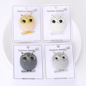Detailed macro view of four owl brooches in gold, silver, and tin with pearl accents