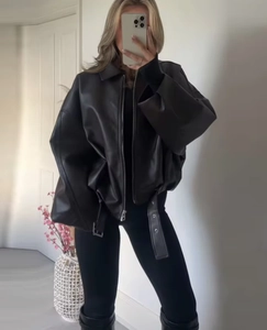 Detail of oversized black faux leather jacket featuring a lapel collar and belted waist hem
