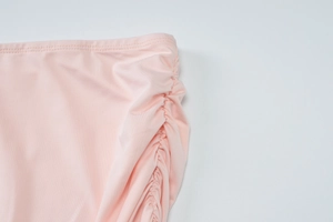 Detailed close-up of pink ruched side seams and textured elastic fabric of the garment
