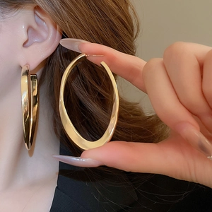 Detail view of large gold oval hoop earrings showing high polished metallic finish on model