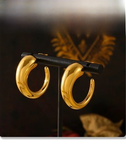 Detailed macro view of C-shaped 18k gold plated hollow earrings on a black display stand