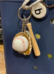 Detailed view of the baseball, glove, and wooden bat charm set hanging on a blue bag