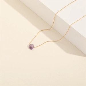 Detailed shot of amethyst heart pendant on a gold chain over minimalist white steps