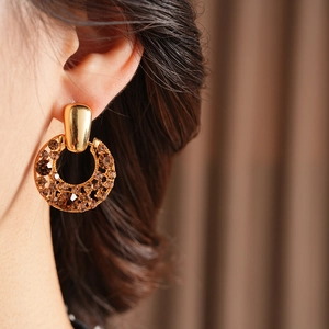 Gros plan de boucles d'oreilles dorées ajourées avec strass marron sur un mannequin