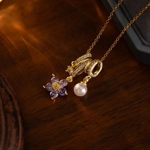 Detail of gold necklace with purple flower zircon pendant and pearl on wood surface
