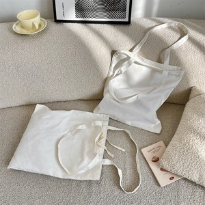 Detailed lifestyle view of minimalist white canvas tote bags on a textured beige sofa