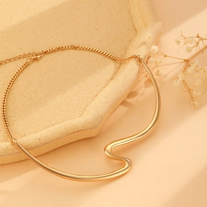 Close-up of golden irregular wavy metal tube necklace on a beige textured tray