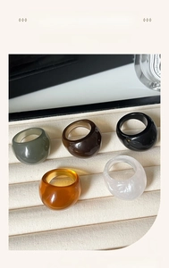 Macro shot of colorful resin rings in emerald, amber, and marble white displayed on beige suede