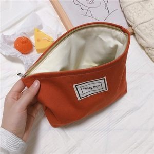 Detail view of orange cotton canvas bag with top zipper and Time To Party woven label