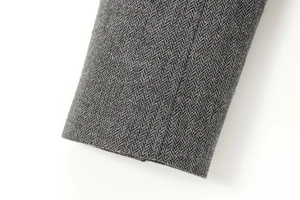 Detailed close-up of grey herringbone fabric texture on double-breasted suit sleeve
