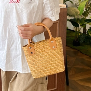 Close-up of a woven straw handbag featuring light brown leather handles and metal rivets
