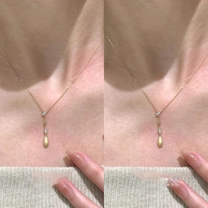 Close-up of golden teardrop pendant with zircon stones on a brushed metal finish necklace