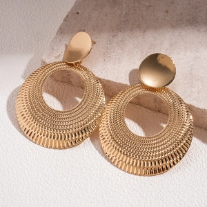 Macro detail of gold metal hollow hoop earrings with sunburst texture on stone